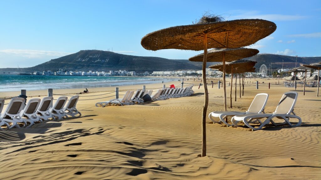 Plage ensoleillée d'Agadir avec des palmiers et des parasols, reflétant le charme relaxant de la ville